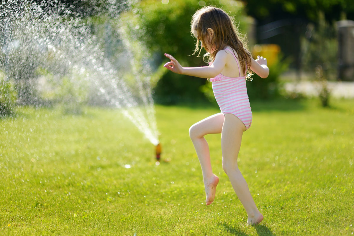 Girl Running Though A Sprinkler In A Backyard Maltby Tree